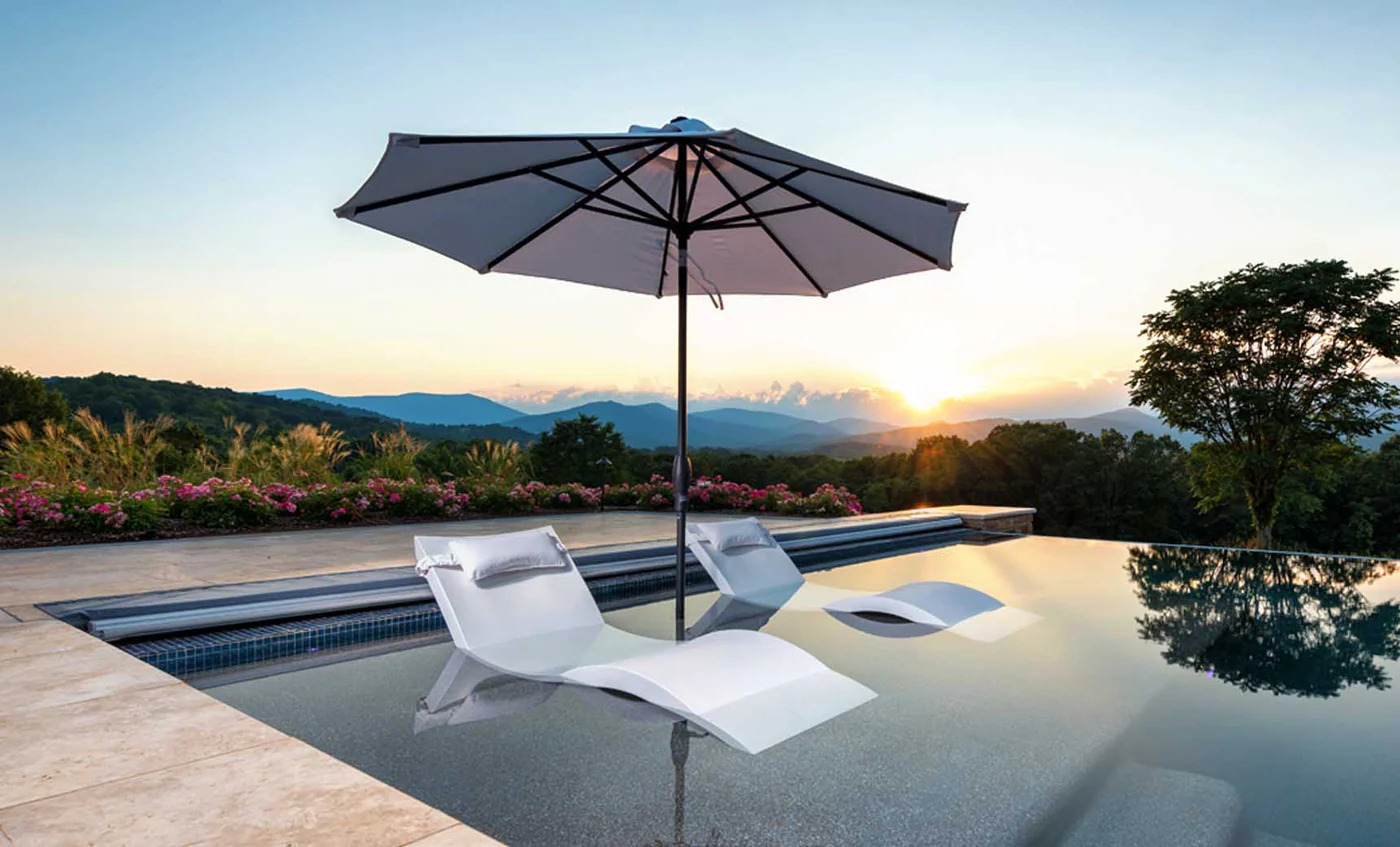 In-water lounge chairs on a sun shelf at the edge of an infinity pool overlooking mountains at sunset